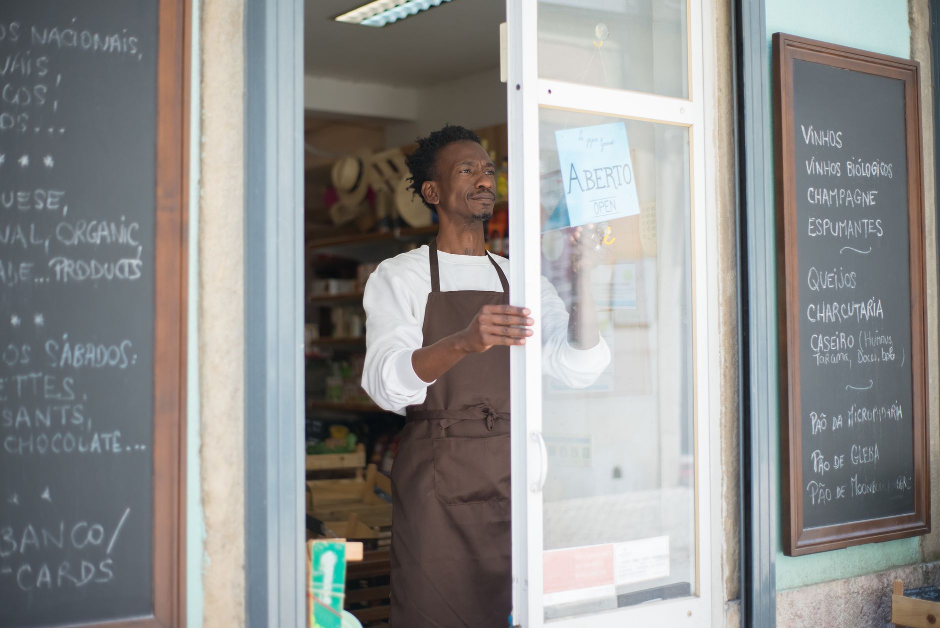 A man in an apron opens a grocery store door in Portugal, ready for business.