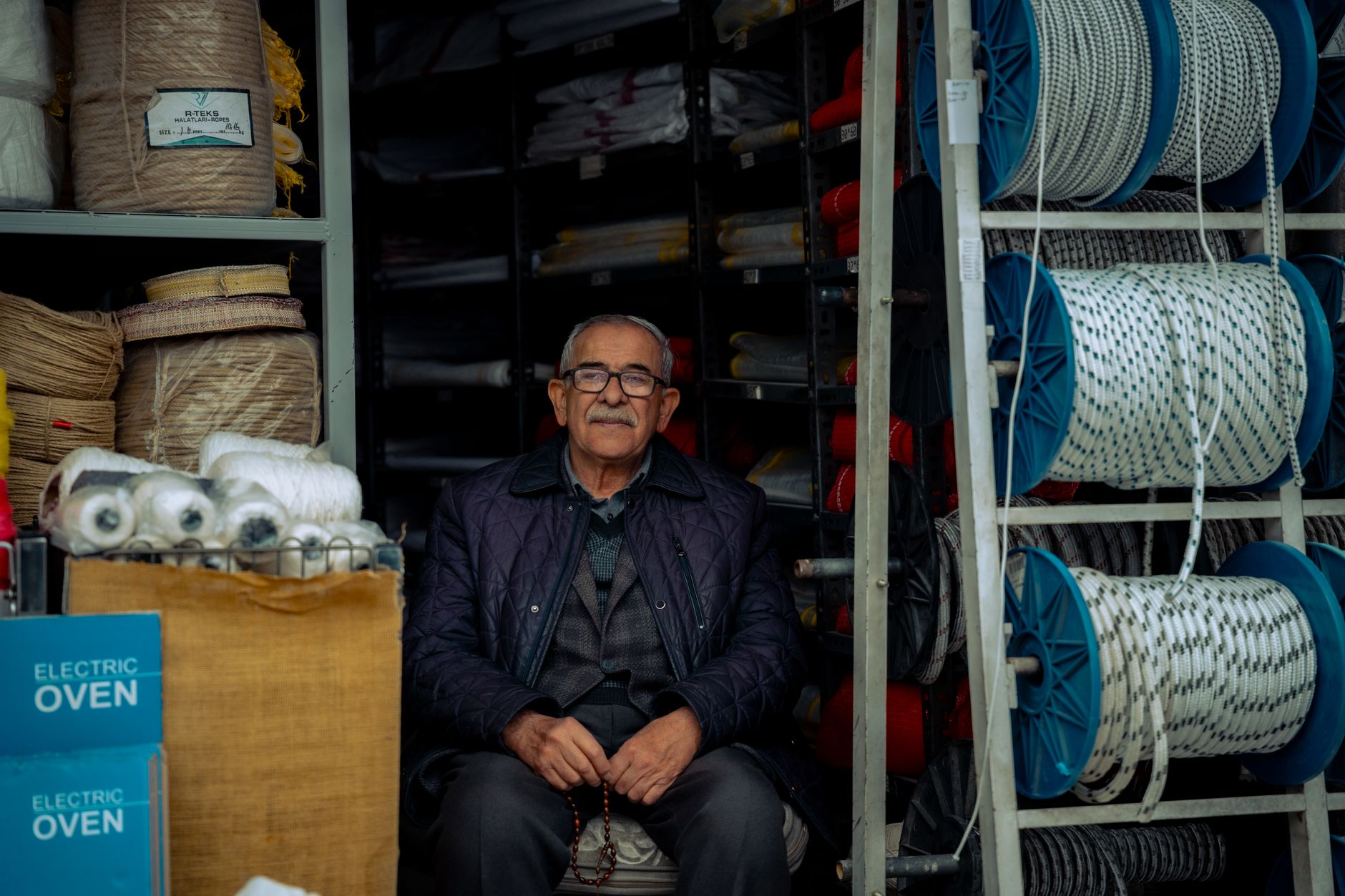 Elderly man sitting in a rope and textile store, exuding warmth and charm.