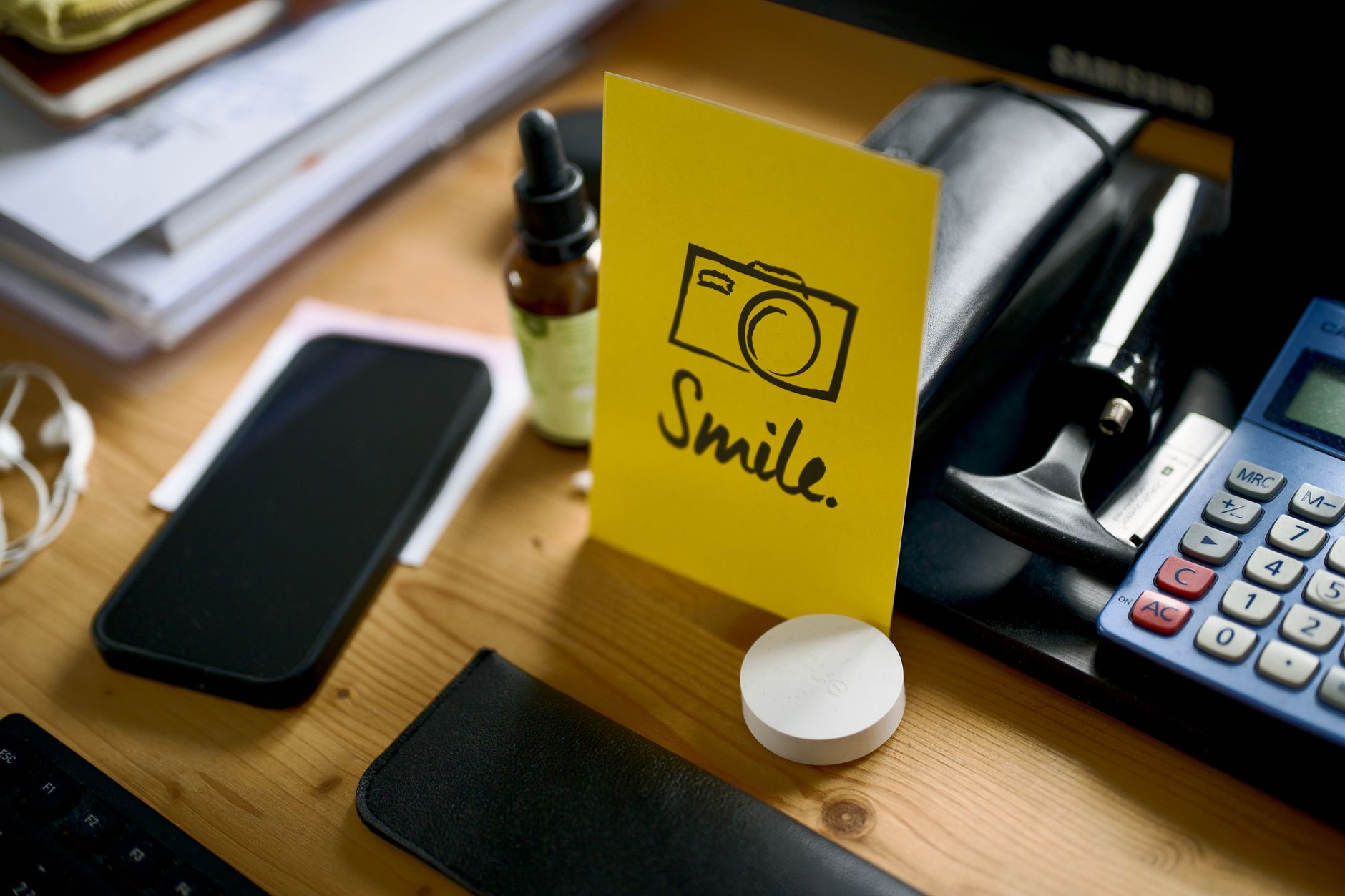 A desk with a smartphone, calculator, and motivational card displaying the word 'Smile'.